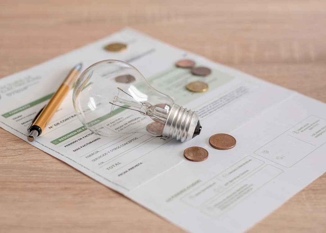 Un bec pus peste factura la energie electrică, pe care se află câteva monede și un pix